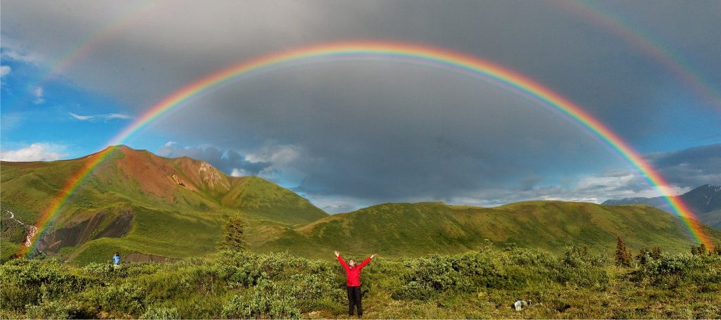 Walker stretching out beneath double rainbow in Wrangell-St. Elias Park, Alaska.